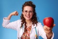 Paediatrist woman giving an apple and showing biceps on blue