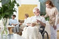 Happy paralyzed senior man in a wheelchair reading a book and a