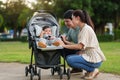 happy parent (father and mother) talking and playing with infant baby in stroller while resting in park