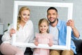 happy parents with adorable little daughter holding white frame and smiling