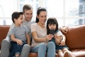Happy parents with cute kids sit on sofa using phone Royalty Free Stock Photo
