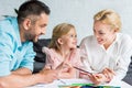happy parents and cute little daughter drawing with colored pencils together