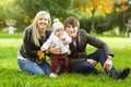 Happy parents with daughter sitting on grass in autumn park Royalty Free Stock Photo