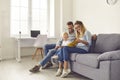 Happy parents and kid sitting on sofa, reading book of stories or looking through family photo album Royalty Free Stock Photo