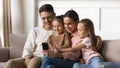 Happy parents with kids daughters relax on sofa using smartphone Royalty Free Stock Photo