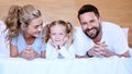 Happy parents with little daughter lying on bed at home. Smiling caucasian girl bonding and enjoying free time with her Royalty Free Stock Photo