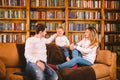 Happy parents playing with small child at Christmas time at home in living room on sofa near large cabinet with books and Royalty Free Stock Photo