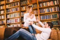 Happy parents playing with small child at Christmas time at home in living room on sofa near large cabinet with books and Royalty Free Stock Photo