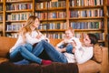 Happy parents playing with small child at Christmas time at home in living room on sofa near large cabinet with books and Royalty Free Stock Photo