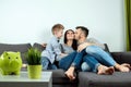 Happy parents and son having fun, tickling sitting together on the sofa, cheerful couple laughing, playing a game with their son, Royalty Free Stock Photo