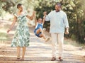 Happy parents swing girl at their hands in the forest during a walk in nature. Cheerful kid having fun while bonding Royalty Free Stock Photo