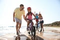 Parents teaching children to ride bicycles on sandy beach near sea Royalty Free Stock Photo