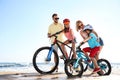 Happy parents teaching children to ride bicycles on beach near sea