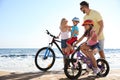 Parents teaching children to ride bicycles on sandy beach near sea Royalty Free Stock Photo