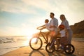 Parents teaching children to ride bicycles on sandy beach near sea at sunset Royalty Free Stock Photo