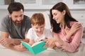 Happy parents with their child reading book on couch at home Royalty Free Stock Photo