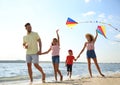 Happy parents and their children playing with kites on beach near sea. Spending time in nature Royalty Free Stock Photo