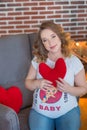 Happy parents-to-be couple looking at a cute red baby shoes for their unborn child, indoors studio portrait Royalty Free Stock Photo