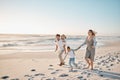 Happy parents walking with their children on the beach. Young family on vacation by the ocean. Children enjoying freedom