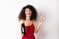 Happy party woman in red dress, laughing and holding bottle of champagne with glass, drinking and having fun Royalty Free Stock Photo