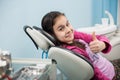 Happy patient girl showing thumbs up at dental office. Medicine, stomatology and health care concept