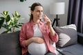 Happy peaceful young pregnant woman drinking water sitting on cozy sofa at home. Beautiful expectant lady have rest in living room Royalty Free Stock Photo