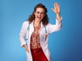 Happy pediatrist woman in white medical robe on blue greeting