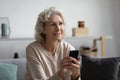 Happy pensive mature lady holding smartphone at home Royalty Free Stock Photo