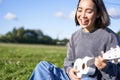 Happy people and hobbies. Smiling asian girl playing ukulele guitar and singing, sitting in park outdoors on blanket Royalty Free Stock Photo