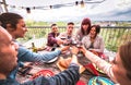 Wide angle view of happy people toasting red wine together at rooftop party in open air villa - Young friends eating bar-b-q food