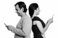 Happy Persian couple smiling while using mobile phone together back to back Royalty Free Stock Photo