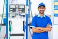 Happy petrol pump worker standing with crossed arms by looking camera at gas filling station - concept of successful