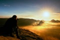 Happy photo enthusiast is enjoying fantastic miracle of nature on cliff on rock. Dreamy fogy landscape bellow.