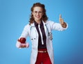 Happy physician woman with dumbbell and apple showing thumbs up