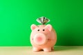 Happy piggy bank with one hundred dollar on color table against green background, space for text