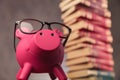 Happy piggy bank wearing glasses looks up near books