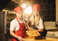 Happy pizza bakers pulling a fresh salami pizza from the stone oven in a box for delivery at italian pizzeria