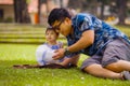 Happy playful Asian Chinese man as loving father enjoying sweet and beautiful baby girl daughter sitting together playing on grass Royalty Free Stock Photo