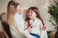 Happy playful little girl daughter playing with positive mother, jumping on sofa, spending time together during Christmas holidays