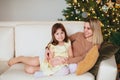 Happy playful little girl daughter playing with positive mother, jumping on sofa, spending time together during Christmas holidays