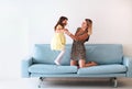 Playful little girl daughter playing with positive mother, jumping on sofa Royalty Free Stock Photo