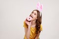 Happy playful teenager girl with brown hair in yellow casual T-shirt with pink bunny ears, biting tasty donut, easter symbol, Royalty Free Stock Photo