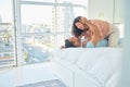 Happy playful young mixed race woman kneeling on top of her boyfriend in bed at home. Romantic couple bonding in their Royalty Free Stock Photo