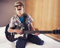 Happy, playing and child with guitar on bed for music lesson with sunglasses at modern home. Fun, rockstar and young boy Royalty Free Stock Photo