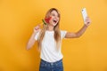 Happy pleased positive young blonde woman jumping isolated over yellow wall background dressed in white casual t-shirt holding Royalty Free Stock Photo