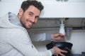 Happy plumber fixing under sink in kitchen Royalty Free Stock Photo