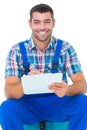 Happy plumber writing on clipboard while sitting on toolbox