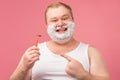 Happy plump man with shaving foam on his face and razor isolated on pink Royalty Free Stock Photo