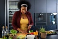 Happy plus size african american woman preparing dinner, chopping vegetables in kitchen Royalty Free Stock Photo