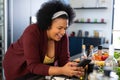Happy plus size african american woman using smartphone, preparing food in kitchen Royalty Free Stock Photo
